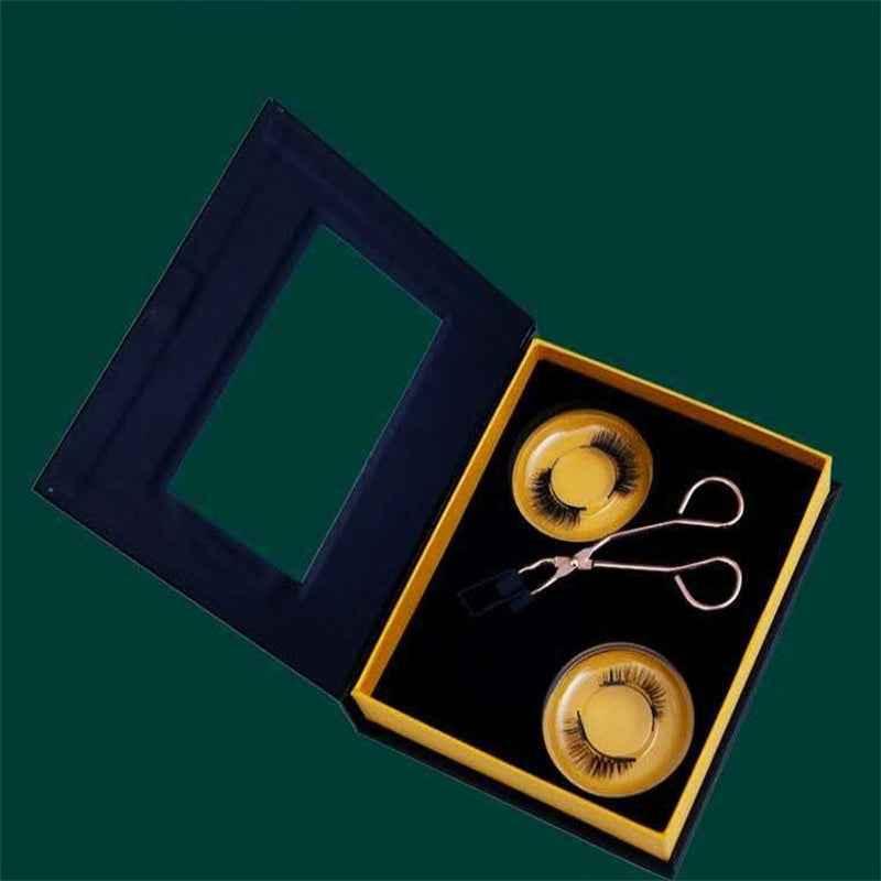 Open black and yellow box with magnetic false eyelashes and silver eyelash applicator tool on dark green background