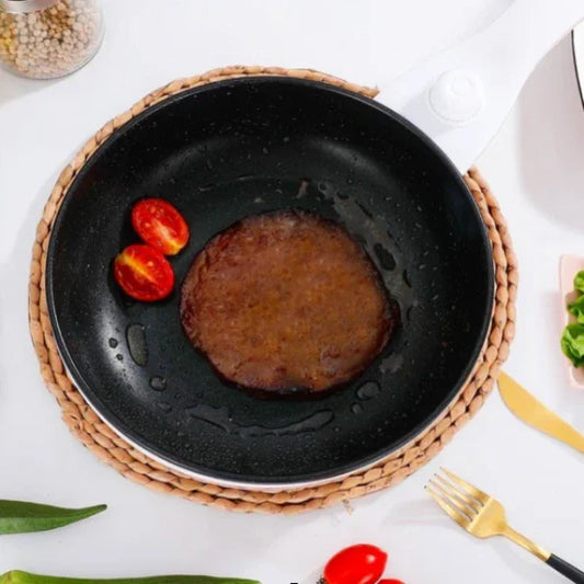 Black frying pan with cooked vegan burger patty and two cherry tomato halves on woven placemat