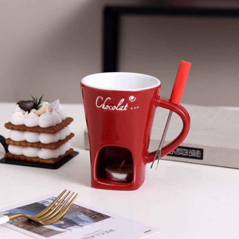 Red ceramic chocolate fondue mug with candle holder and fork on table with dessert
