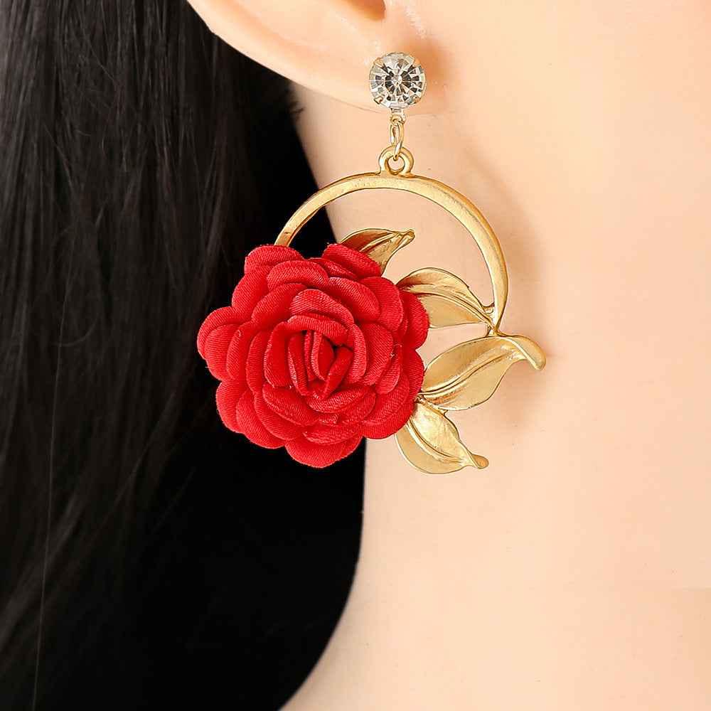 Close-up of a gold hoop earring with red fabric rose and gold leaves worn on ear